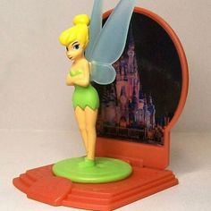 a toy tinkerbell is standing in front of a mirror with a castle behind it