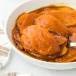 a white bowl filled with cooked chicken and gravy on top of a table