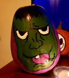 a pumpkin with a face painted on it sitting next to a bowl and computer monitor