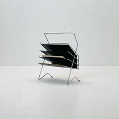 a stack of books sitting on top of a metal stand next to a white wall