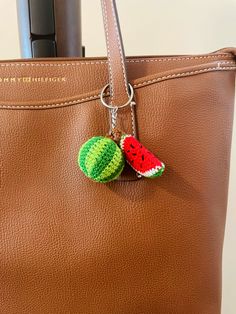 a brown purse with two crocheted watermelon charms hanging from the handle