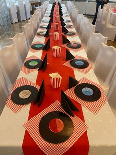 a long table is set up with red and black placemats, cupcakes, and vinyl records