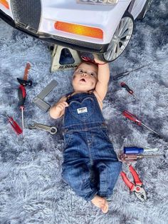 a baby laying on the ground next to a car with tools all around it's body