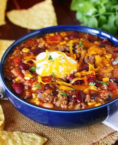 a blue bowl filled with chili and cheese next to tortilla chips on a table