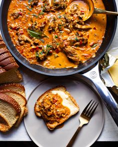 a skillet filled with meat and cheese next to sliced bread on top of a table