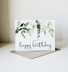 a card with the words happy birthday written in black ink and green leaves on it