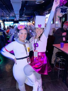 two women dressed in costumes pose for the camera at a party with balloons and decorations