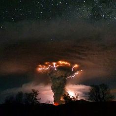 a very tall tower with lots of lightning coming out of it's side and some trees in the foreground