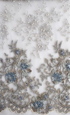 an embroidered fabric with silver and blue flowers on the bottom, along with pearls in the middle