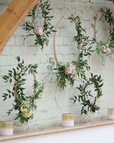 flowers and greenery are arranged on the wall above candles in front of a brick wall