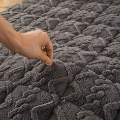 a person is touching the edge of a bed with a gray blanket on top of it