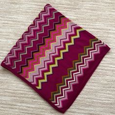 a pink and yellow zigzag pattern on a red square pillow sitting on top of a white carpet