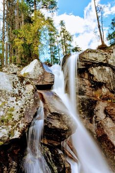 there is a waterfall in the middle of some rocks and trees on the other side