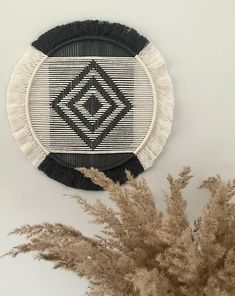 a black and white wall hanging on the side of a wall next to dried grass