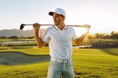 a man holding a golf club in his hands while standing on a green field with the sun behind him