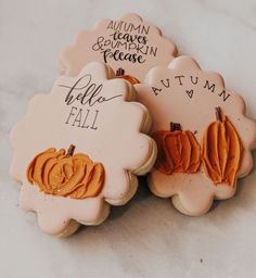 three decorated cookies sitting on top of a white tablecloth covered table with writing and pumpkins