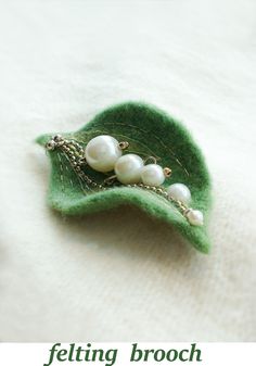 a brooch with pearls is sitting on top of a green leaf and has the words felting brooch written below it