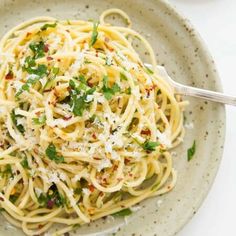 a plate of spaghetti with parmesan cheese and herbs on the side, ready to be eaten