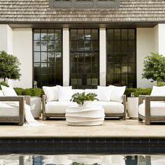 a white couch sitting next to a swimming pool in front of a house with large windows