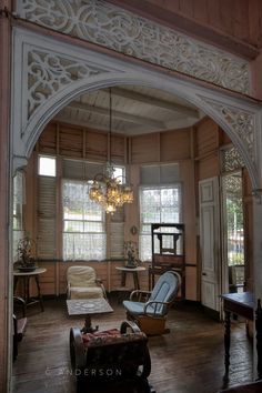 an arched doorway leads to a living room with chairs and tables in it, along with two windows