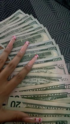 a woman's hand with pink fingernails on top of twenty dollar bills