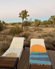 two lounge chairs sitting on top of a wooden deck next to a desert landscape with cacti