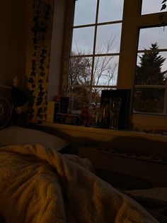 an unmade bed in front of a window with the sun shining through it and trees outside