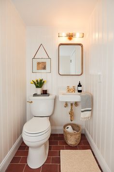 the bathroom is decorated in white and has brown tile on the floor, along with a gold framed mirror above the toilet