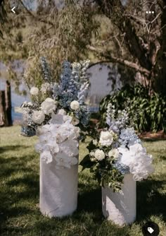 two white vases with blue and white flowers on the grass next to each other