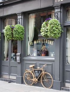 a bicycle is parked in front of a storefront with flowers hanging from the windows