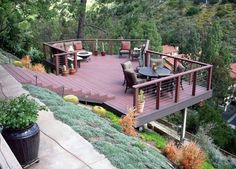 a wooden deck with chairs and tables on it next to a hillside covered in trees