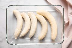 four peeled bananas in a glass dish on a marble counter top with pink linens