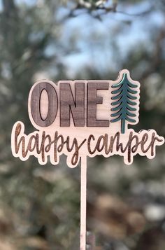 a one happy camper wooden sign sitting on top of a stick in front of some trees