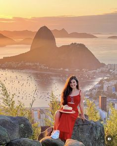 a woman in a red dress is sitting on some rocks and posing for the camera