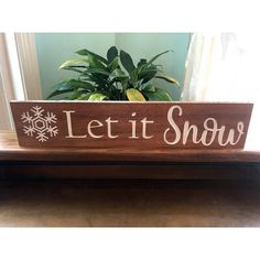 a wooden sign that says let it snow next to a potted plant on a table