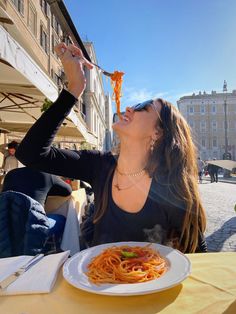 a woman sitting at a table eating spaghetti with her hands in the air and looking up into the sky