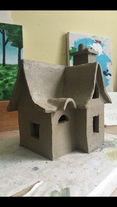 a clay house sitting on top of a table next to some paintbrushes and an easel