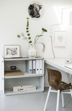 a white desk with books and plants on it next to a wall mounted art piece