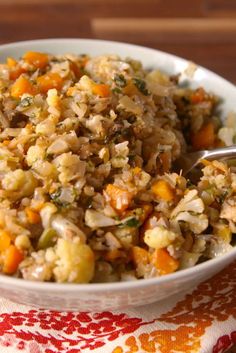 a white bowl filled with rice and carrots on top of a wooden table next to a fork