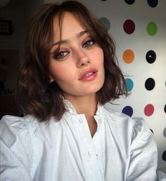 a close up of a person wearing a white shirt with polka dots on the wall behind her