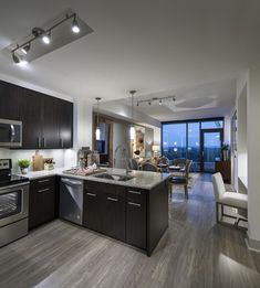 an open kitchen and living room area with wood flooring, stainless steel appliances and large windows