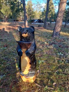 a bear statue sitting in the middle of a forest next to some trees and grass