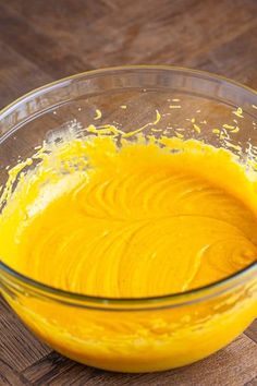 a glass bowl filled with yellow batter on top of a wooden table