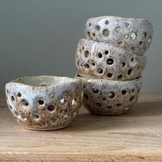 four ceramic bowls sitting on top of a wooden table next to each other with holes in them