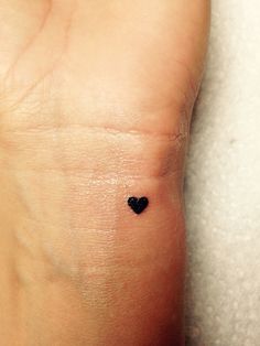 a small black heart tattoo on someone's left foot