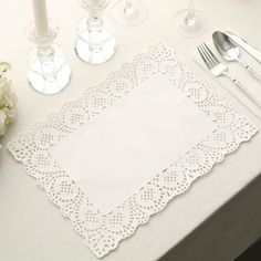 a place setting with white flowers and silverware on a table cloth, surrounded by wine glasses