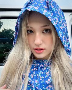 a woman with long blonde hair wearing a blue floral print hoodie and looking at the camera