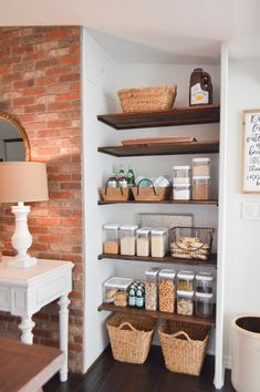 an organized pantry with baskets, food and other items on the shelves in front of a brick wall