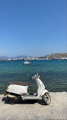 a motor scooter parked on the beach next to the ocean with boats in the water