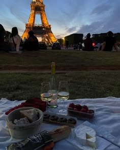 the eiffel tower is lit up at night, with food and wine in front